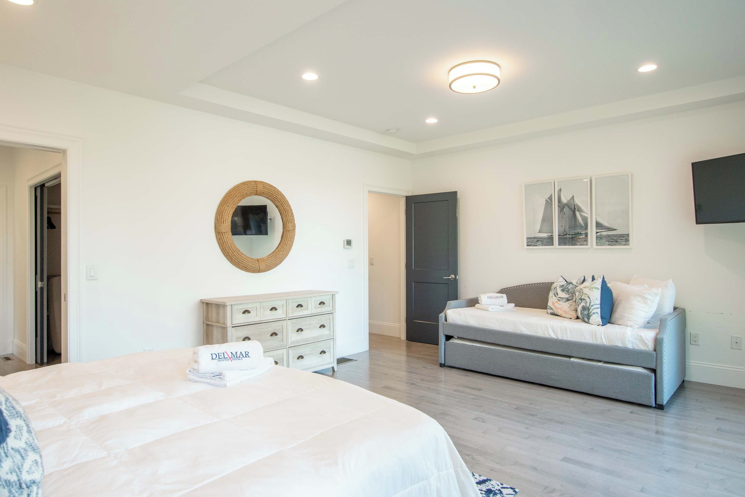 A bedroom with a bed, a dresser, a door, and a wall-mounted TV.
