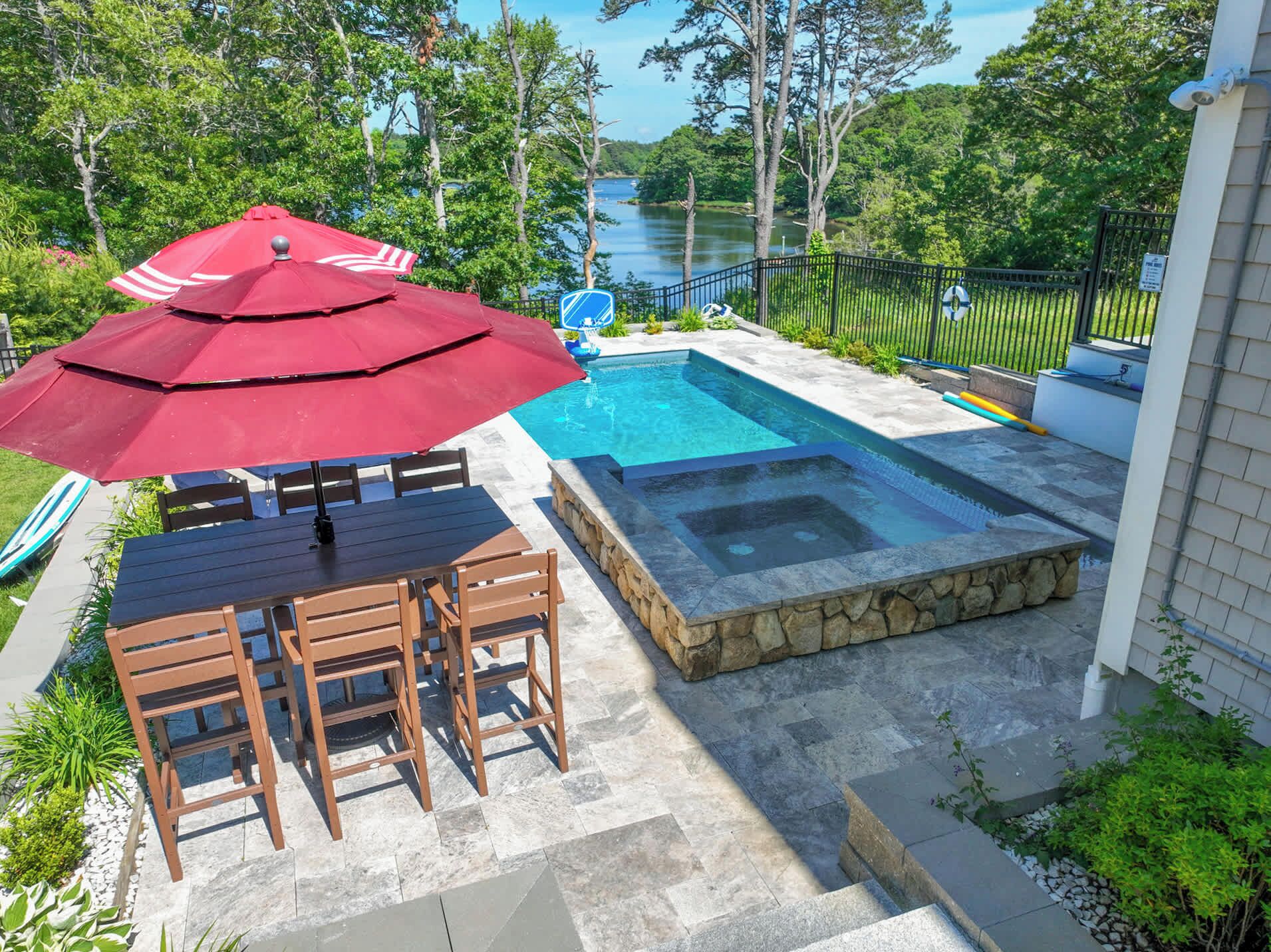 A backyard with a swimming pool, a hot tub, and a dining area with a table and chairs.