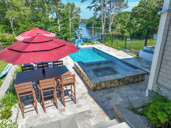 A backyard with a swimming pool, a hot tub, and a dining area with a table and chairs.