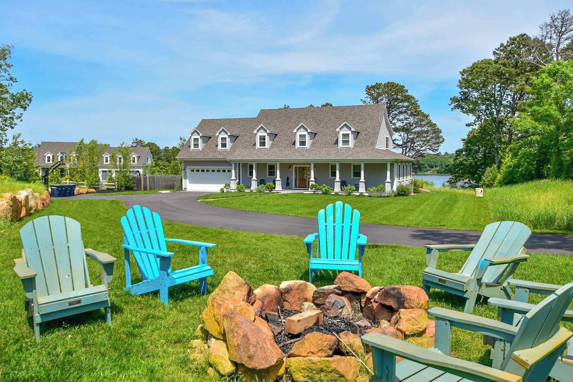 Une grande maison dotée d’un porche, d’un foyer extérieur et de trois fauteuils Adirondack.