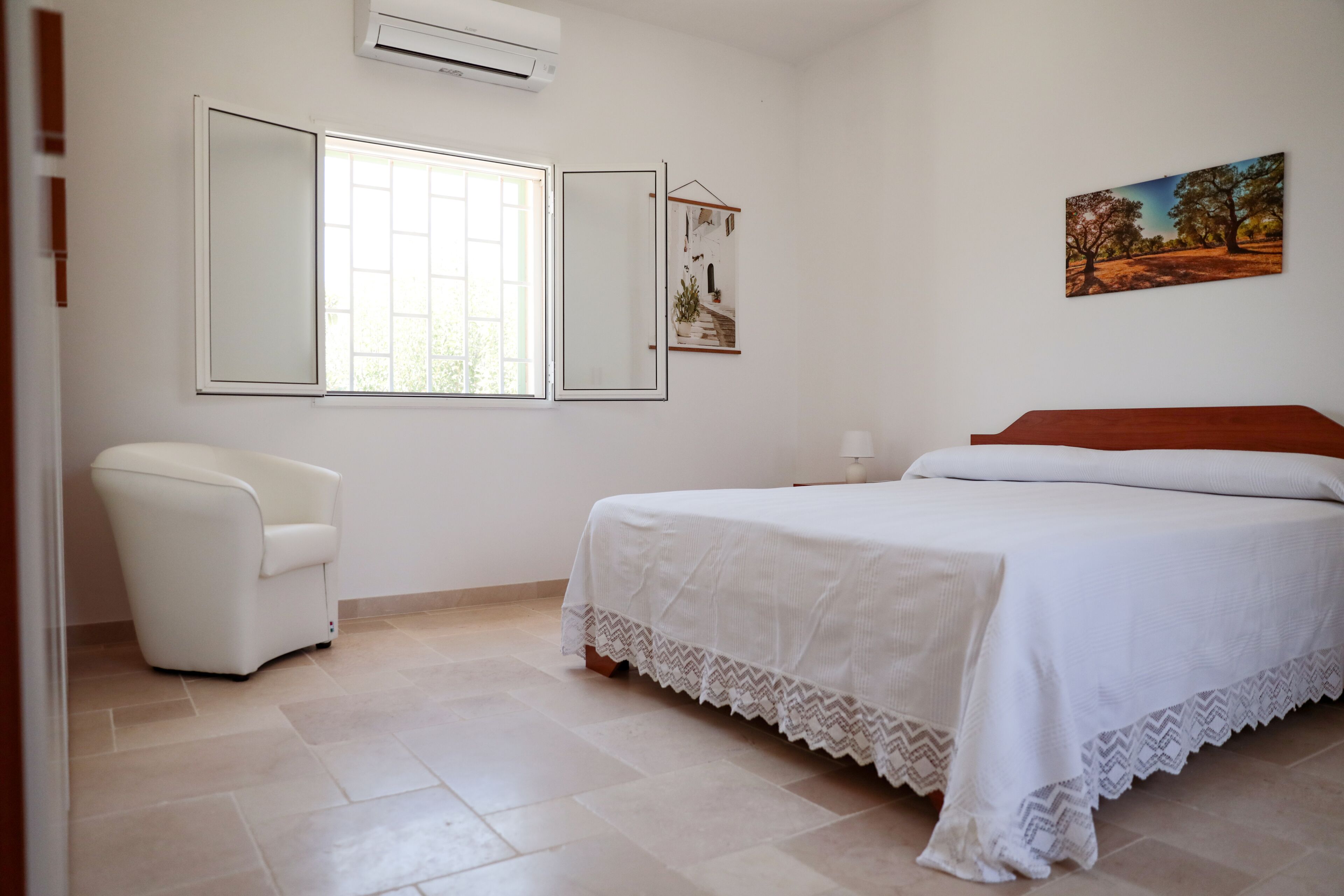 Un dormitorio con cama, una silla, un ventanal y un espejo adosado a la pared.