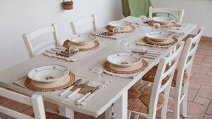 Een net gedekte eettafel met witte stoelen, geweven placemats en blauw-witte borden.