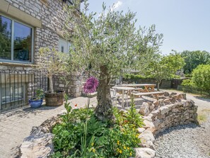 A stone building with a garden featuring a tree, potted plants, and a wooden table and chairs. - Old Watermill (Grange-over-Sands)