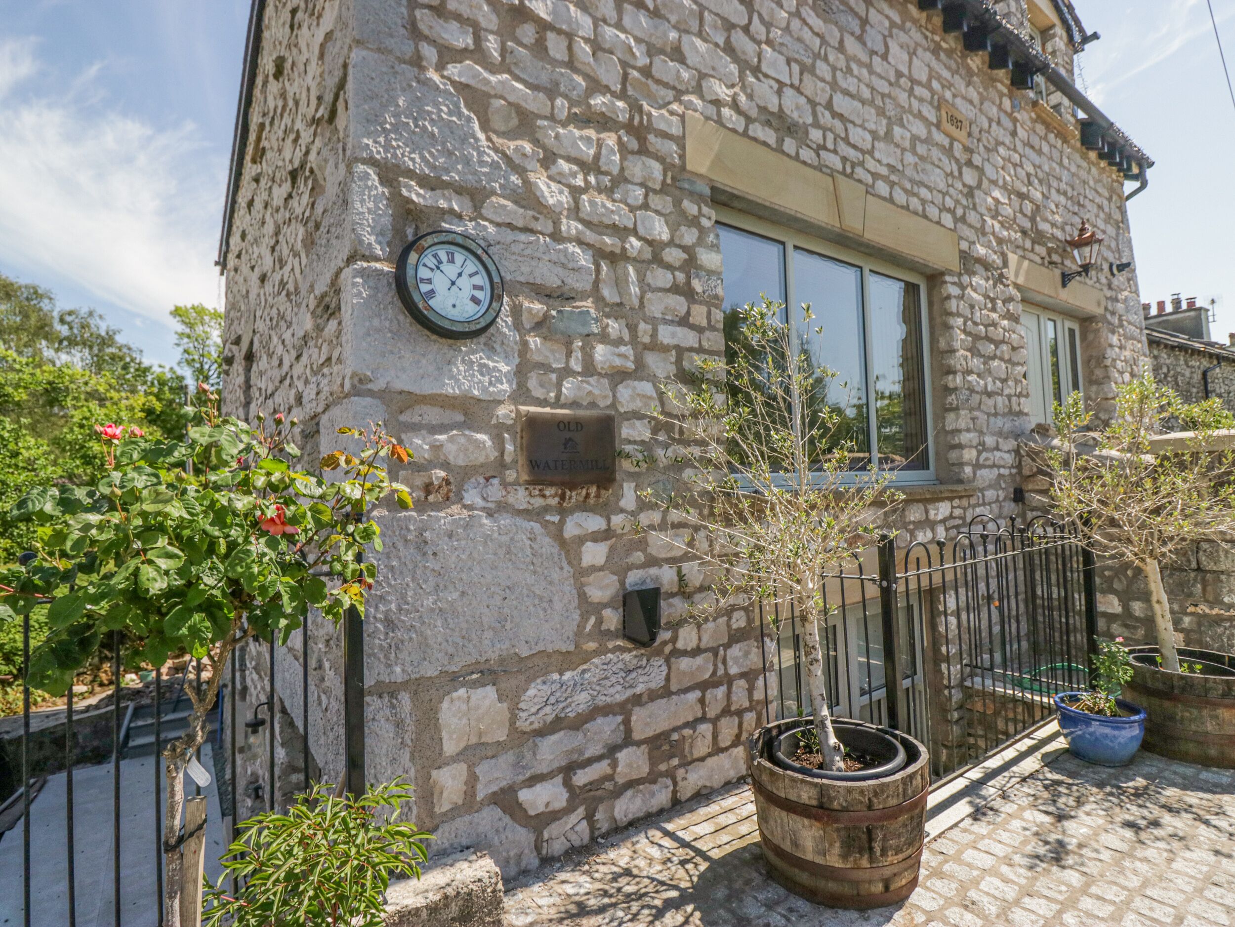 A stone building with a clock, a window, and a sign that reads "Old Watermill".