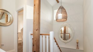 A staircase with white railings and a wooden post, leading to a room with a mirror and a hanging light fixture. - Old Watermill (Grange-over-Sands)