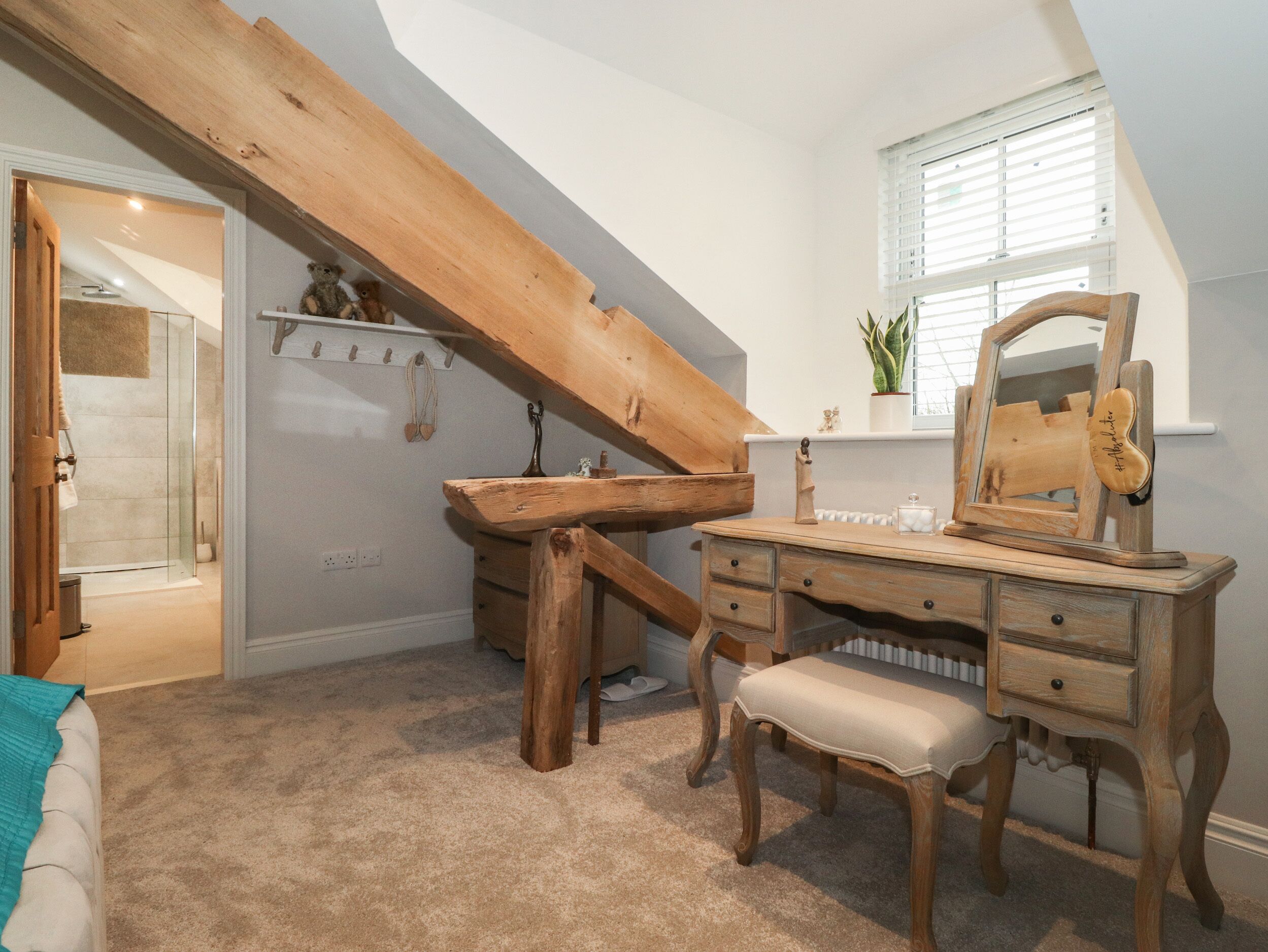 A bedroom with a wooden desk, a bench, a mirror, and a window with blinds.