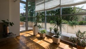 Una habitación con ventanas amplias, suelo de madera y varias plantas en macetas.