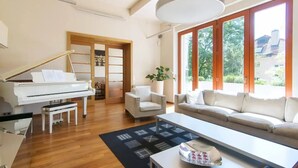 Un salón amplio con un piano de cola, un sofá, una mesa de centro y grandes ventanales con vistas al exterior.