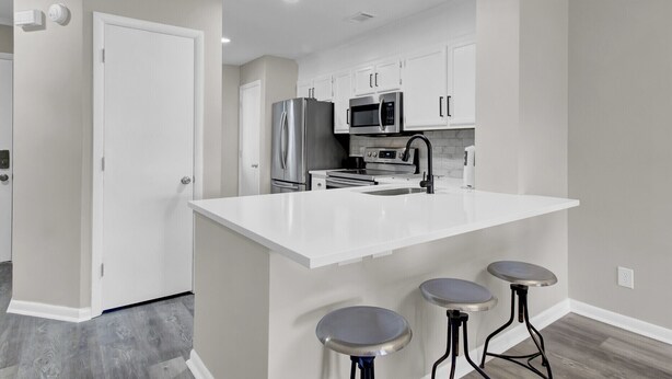 A modern kitchen with white cabinetry, stainless steel appliances, a central island with bar stools, and recessed ceiling lighting.