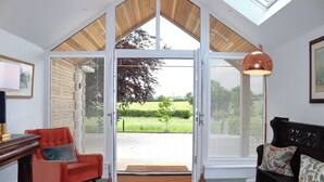 Quarto com uma grande porta de vidro deslizante que dá para um jardim, uma poltrona vermelha, um banco de madeira e uma mesa com abajur.