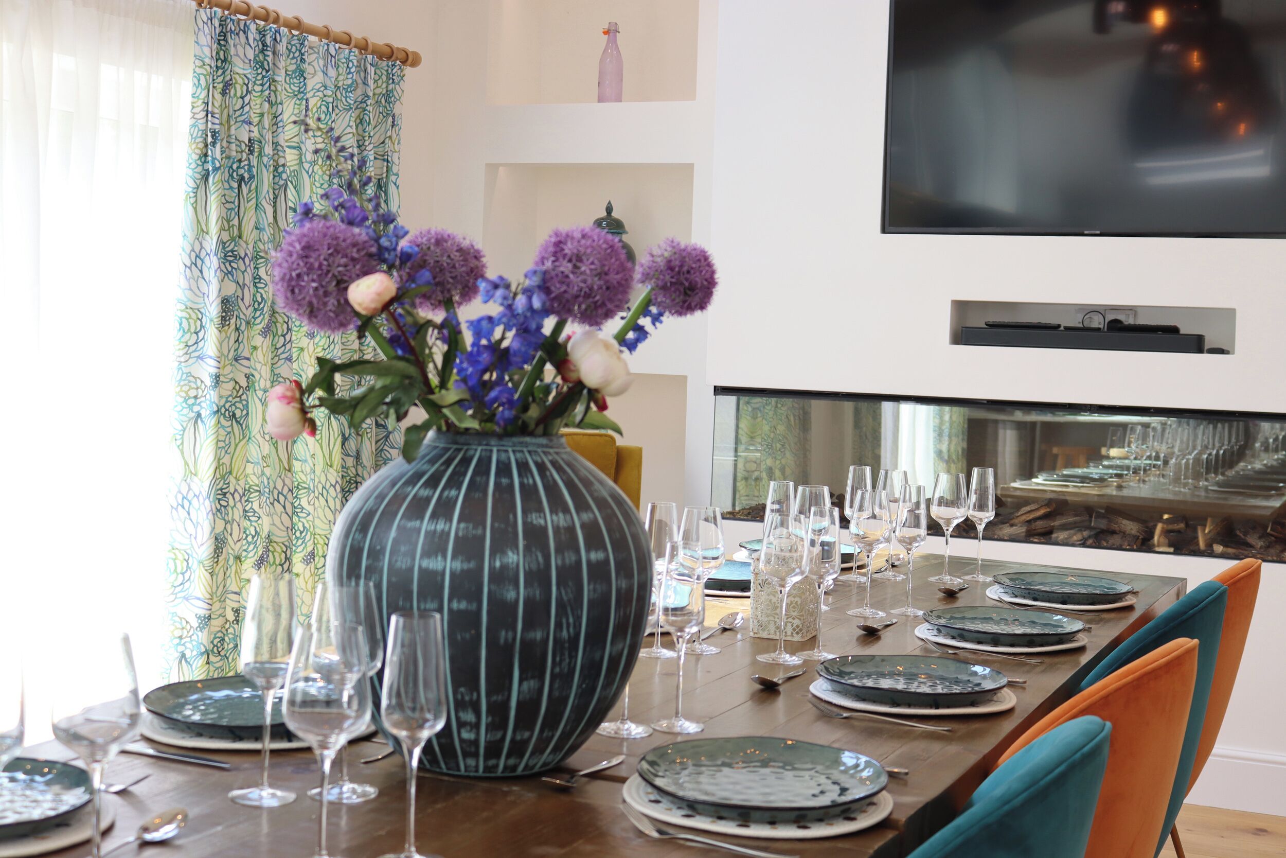 A dining table set with plates, glasses, and a large vase with flowers.
