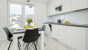 Moderni keittiö, jossa on valkoiset kaapit, musta työtaso sekä ruokailutila, jossa on mustat tuolit ja pöytä.