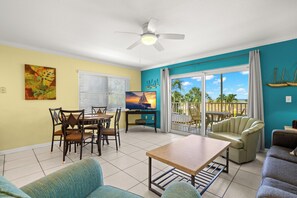 A living room with a dining area, a television, a ceiling fan, and a view of the outdoors.