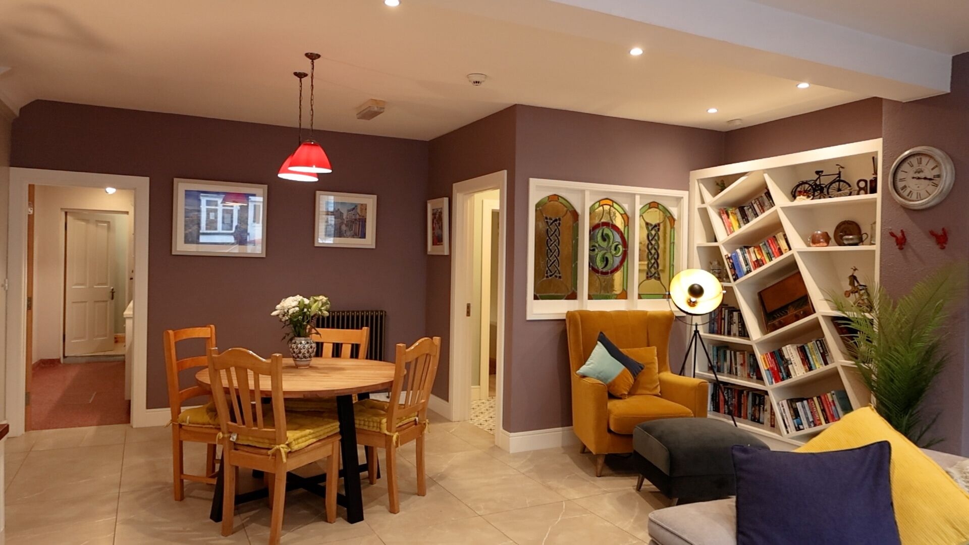 Een woonkamer met een eettafel, stoelen, een bank, een boekenkast en een klok aan de muur.