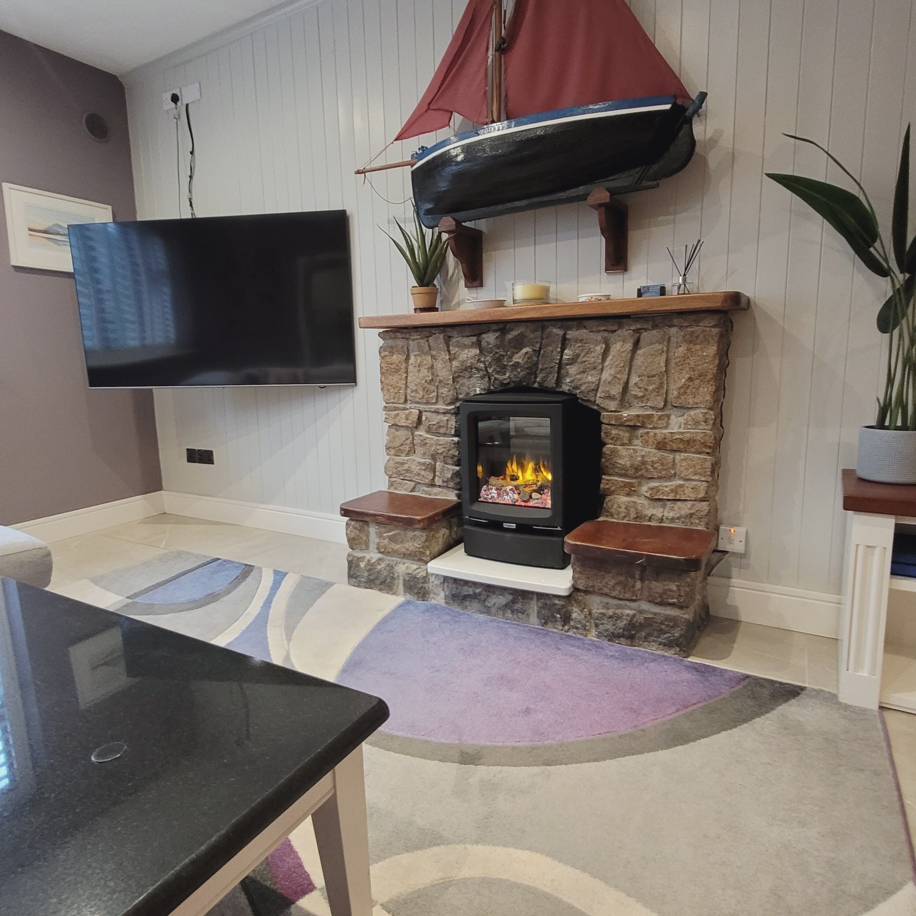 A living room with a stone fireplace, a mounted flat-screen TV, and a sailboat decoration.