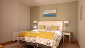 A bedroom with a bed, two bedside tables, a nightstand, a radiator, and a painting on the wall. - Ryans Roundstone Retreats Quayside Luxury Apt (Roundstone)
