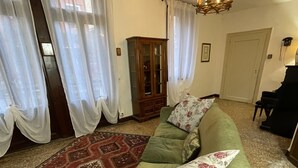 A living room with a green sofa, patterned rug, wooden cabinet, and a chandelier. - LIONS VENICE Guest House (Venice)