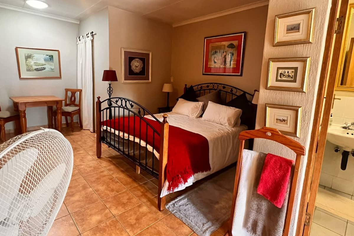 Un dormitorio con cama, una silla, un escritorio y un baño visible a través de una puerta abierta.