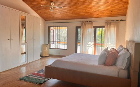 A bedroom with a wooden ceiling, a bed with pillows, a wardrobe, and a window with curtains.