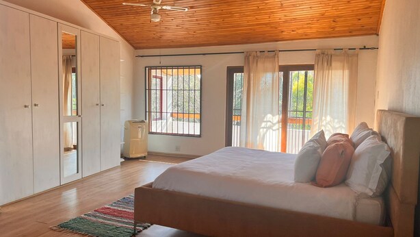 Un dormitorio con techo de madera, una cama con almohadas, un armario y una ventana con cortinas.
