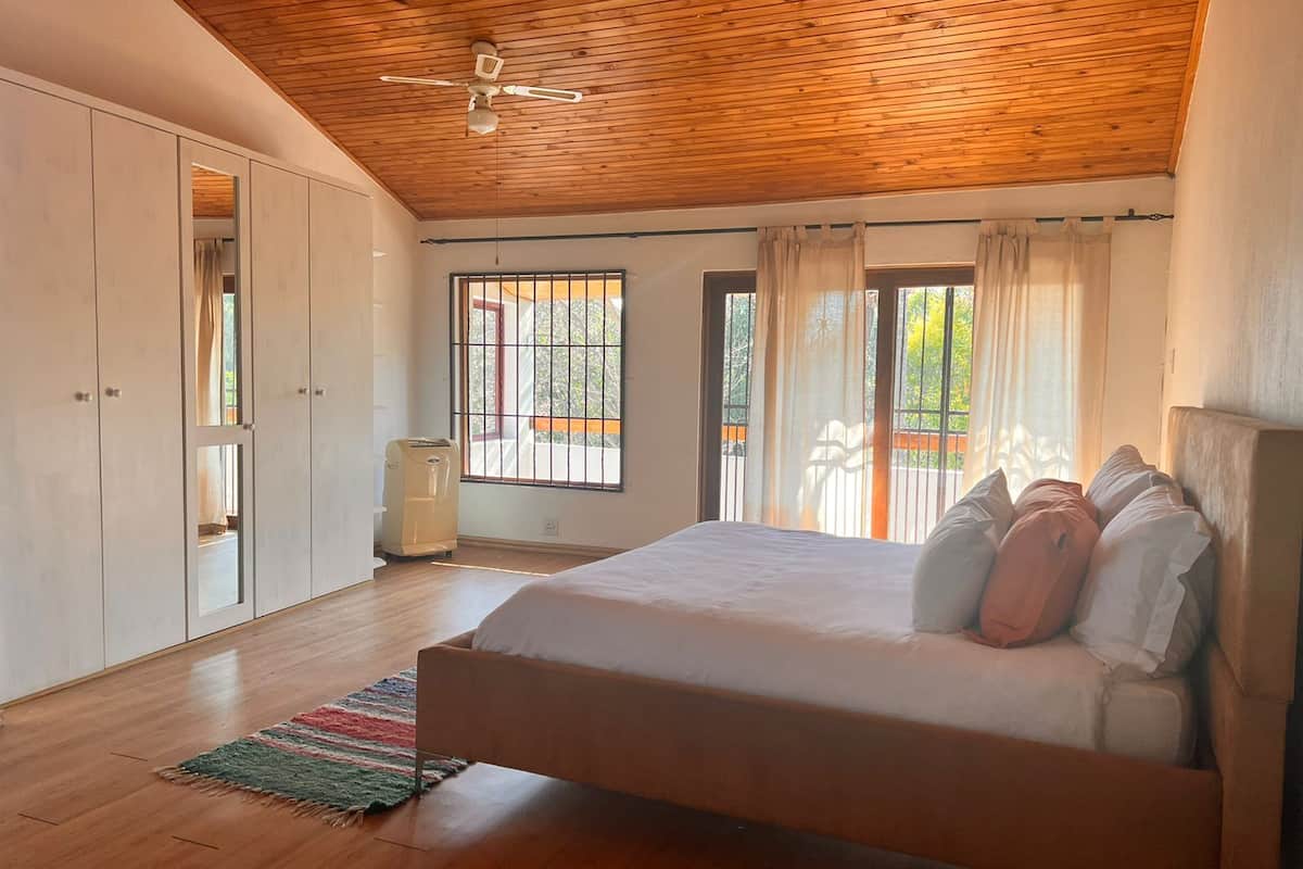 Un dormitorio con techo de madera, una cama con almohadas, un armario y una ventana con cortinas.