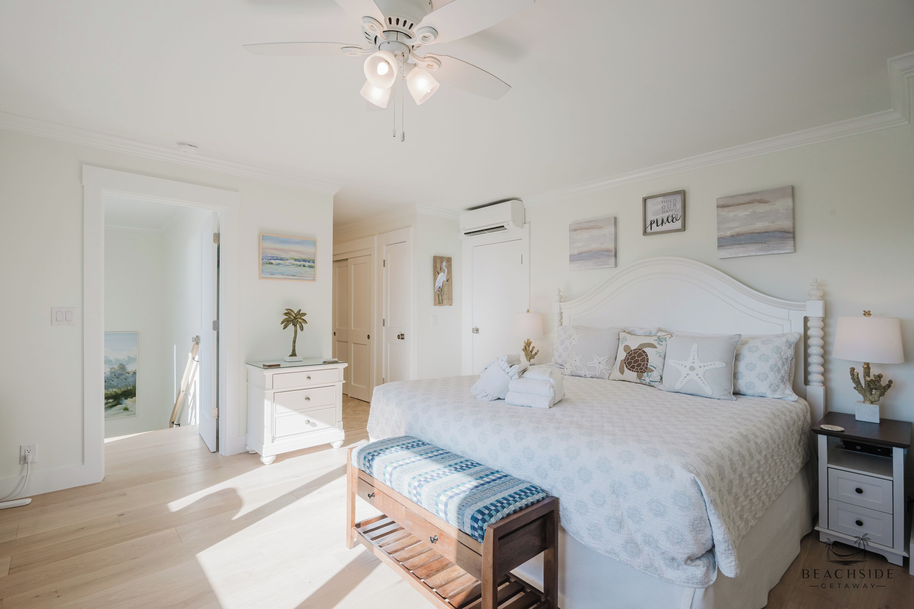 A bedroom with a bed, bedside tables, a bench, a ceiling fan, and artwork on the walls.