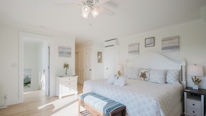 A bedroom with a bed, bedside tables, a bench, a ceiling fan, and artwork on the walls. - 50 Ocean Club-"Ocean Watch" Prime Beachfront Condo (Hilton Head Island)