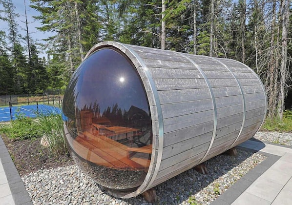 A cylindrical structure with a reflective surface, surrounded by gravel and trees.