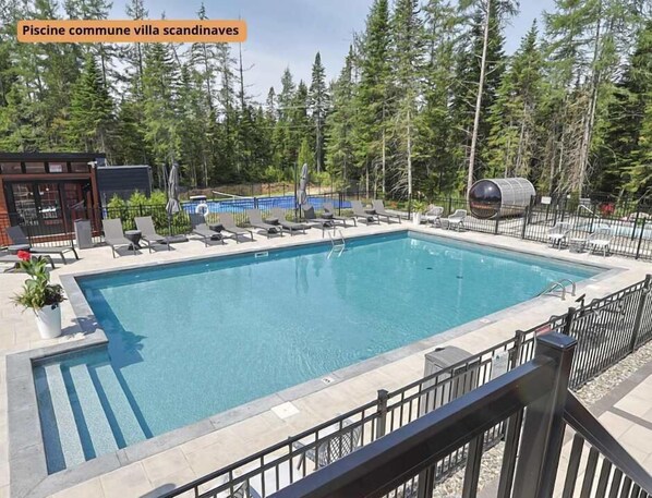 Piscina com espreguiçadeiras, churrasqueira e um fundo arborizado.