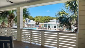 Ein Balkon mit Blick auf einen Swimmingpool, Palmen und ein Gebäude mit einem hellblauen Dach.