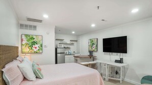 A bedroom with a bed, a desk, a TV, and a kitchenette. - 529 Sunsuite (Fripp Island)