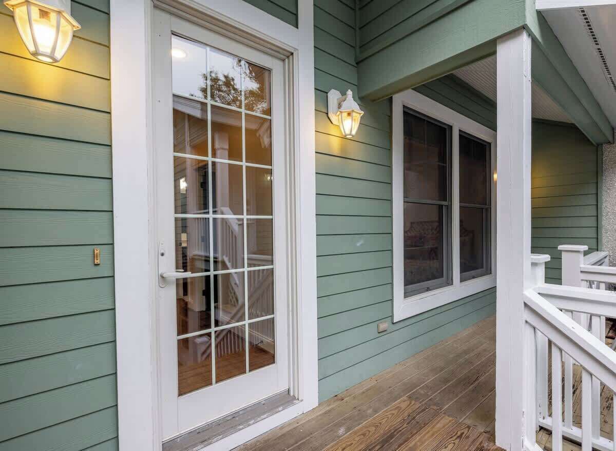 Een veranda met een witte balustrade, een groene buitenmuur en een witte deur met een raam.