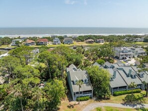 A coastal residential area with houses, dense greenery, and a view of the ocean.