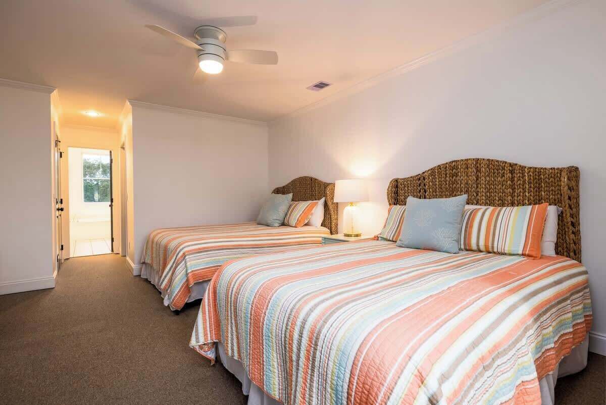 A bedroom with two beds, a ceiling fan, and a door leading to another room.