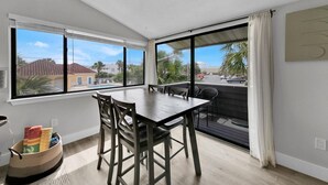 A room with a dining table, chairs, a window with blinds, a view of the outside, and a wall-mounted artwork. - 1BA/1BA Miramar Beach, Inquire for Monthly Rates (Miramar Beach)