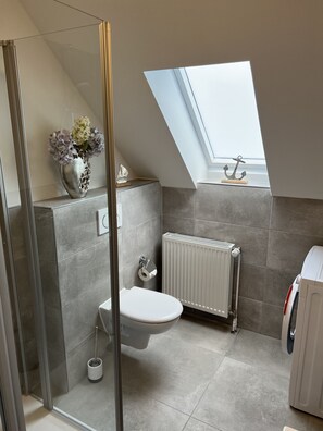 A modern bathroom with a skylight, a toilet, a radiator, and a shower area. - Ferienwohnung Meischen (Bad Zwischenahn)