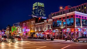 A brightly lit urban street scene with various commercial buildings, including a hotel with a neon sign.