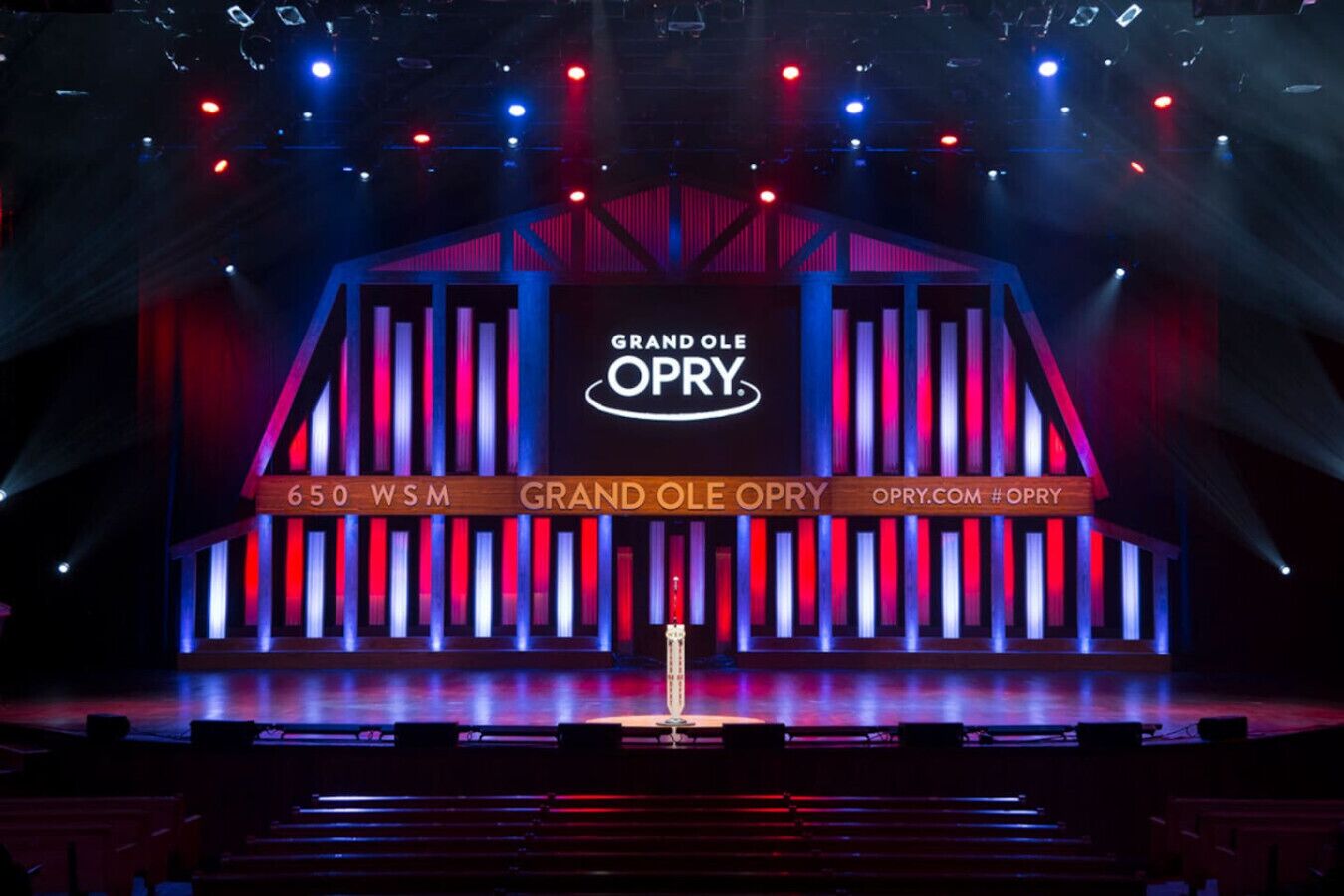 A stage with a large screen displaying "Grand Ole Opry" branding, a podium, and stage lights.