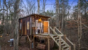 A wooden cabin with a deck and stairs, surrounded by trees.