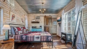 A cozy cabin-style bedroom with a wooden bed, a dresser, and a window with curtains.