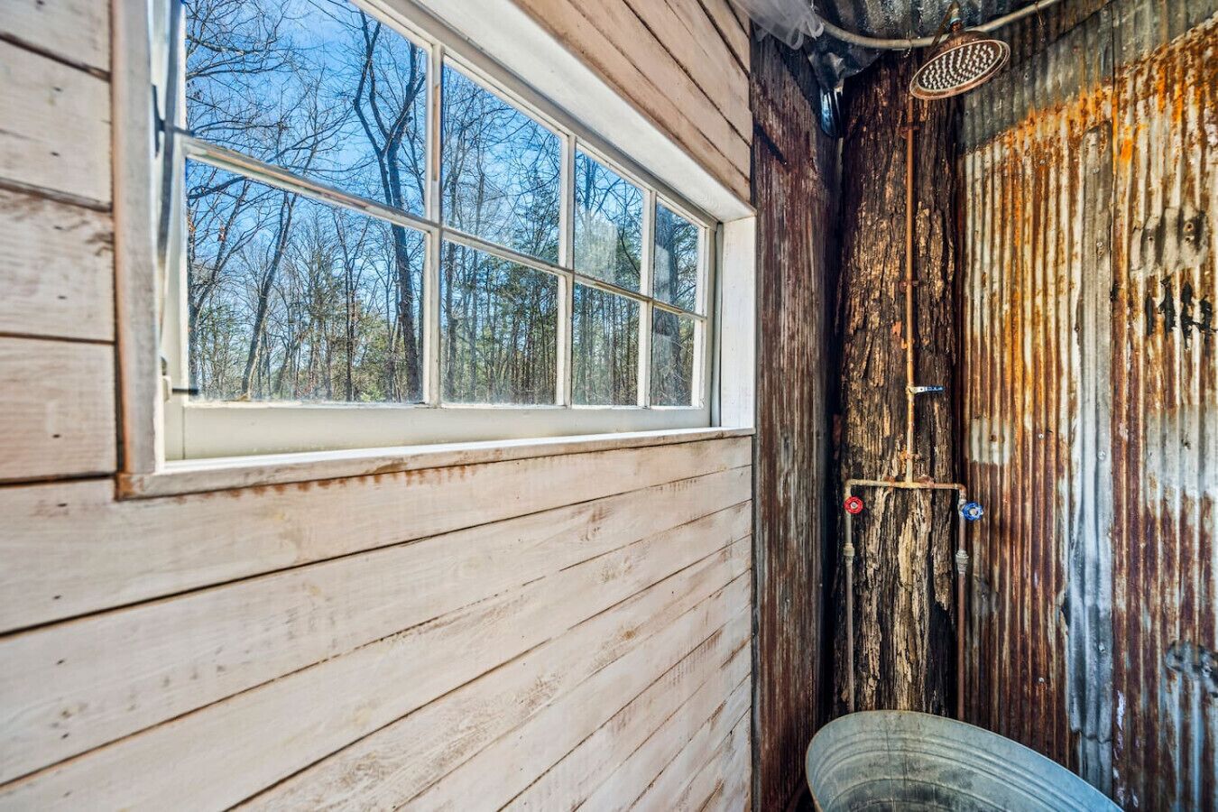 A rustic cabin with a large window, wooden walls, and a metal door with a shower.