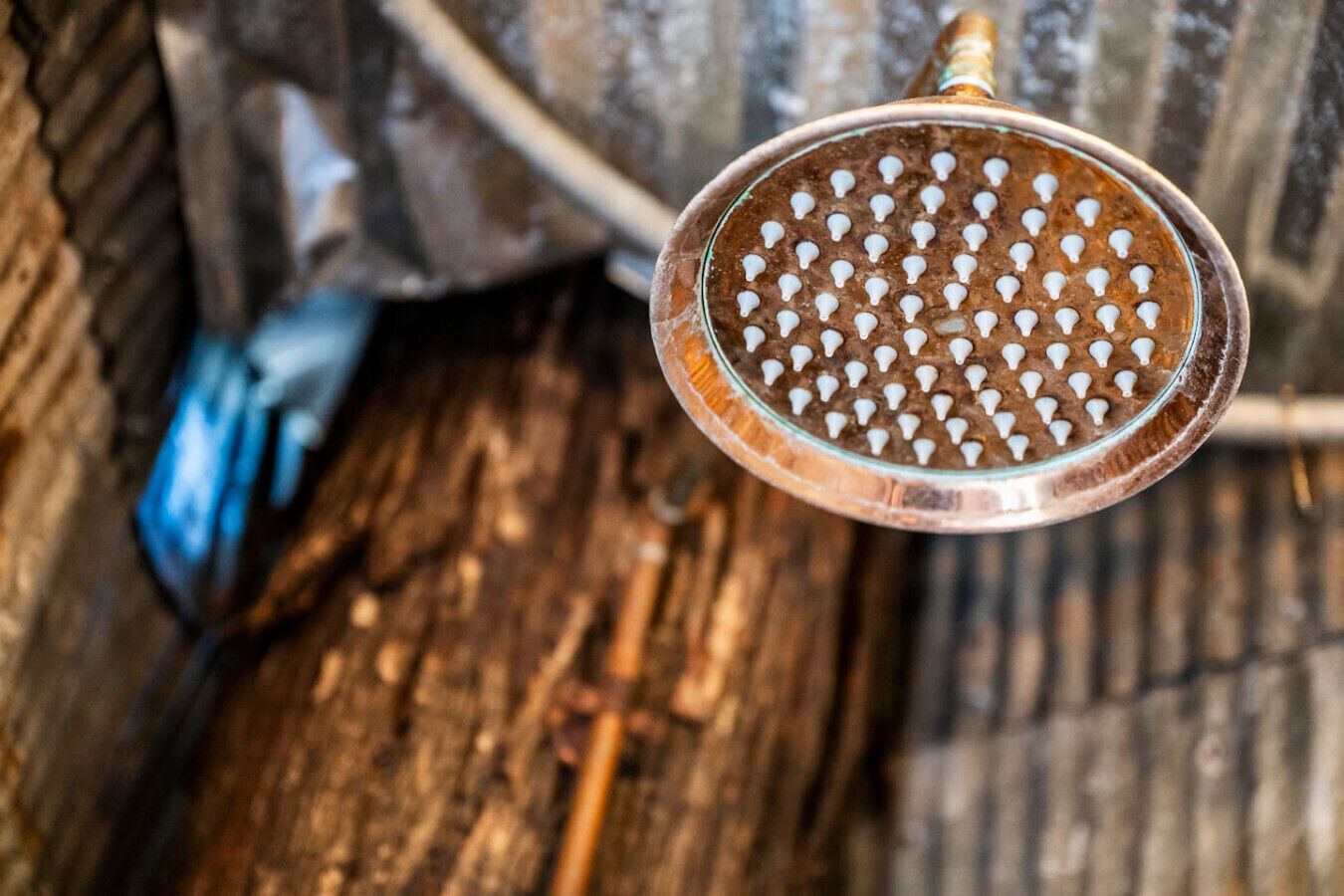 Un objet métallique à surface perforée, qui pourrait être un pommeau de douche, est suspendu à une structure dont l’arrière-plan est en bois.