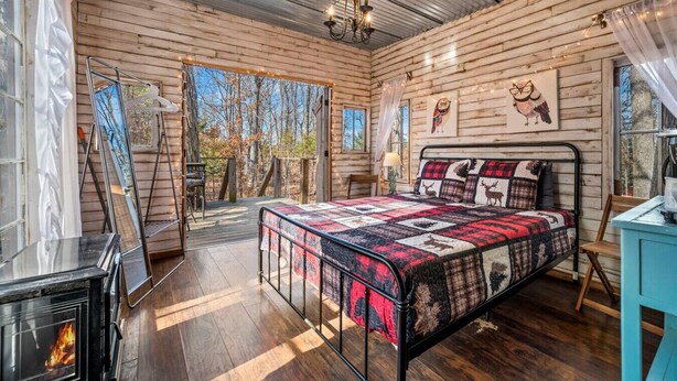 A cozy cabin bedroom with a large bed, a fireplace, and a view of the forest.
