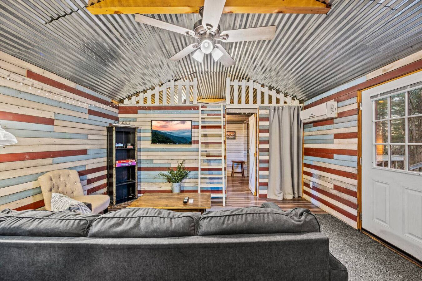 A cozy living room with a sofa, a coffee table, and a TV. There is a ceiling fan and a window.