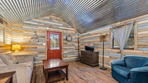 L’intérieur d’un chalet accueillant, avec un plancher en bois, une porte rouge, un téléviseur posé sur une commode, un canapé et une lampe.