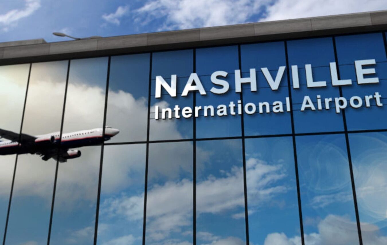 The exterior of the Nashville International Airport with a clear sky and a plane in flight.