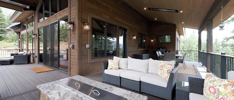 Un espacio al aire libre techado con una chimenea de piedra, mobiliario de mimbre y una parrilla.