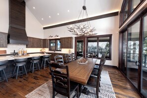 A modern kitchen with dark wood cabinetry, a large island with bar stools, and a dining area with a wooden table and chairs.