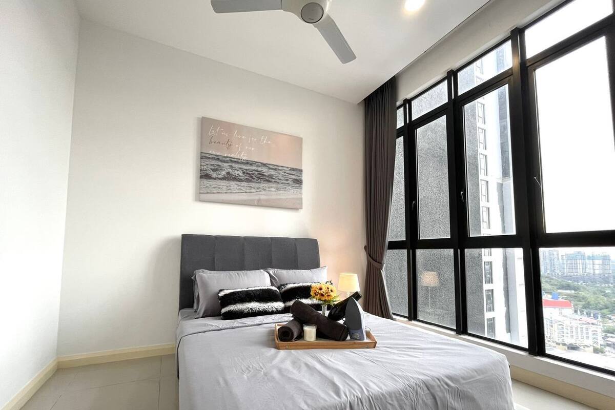 Ein modernes Hotelzimmer mit einem großen Bett, einem Deckenventilator, Blick auf die Stadt durch große Fenster und einem Wandbild.