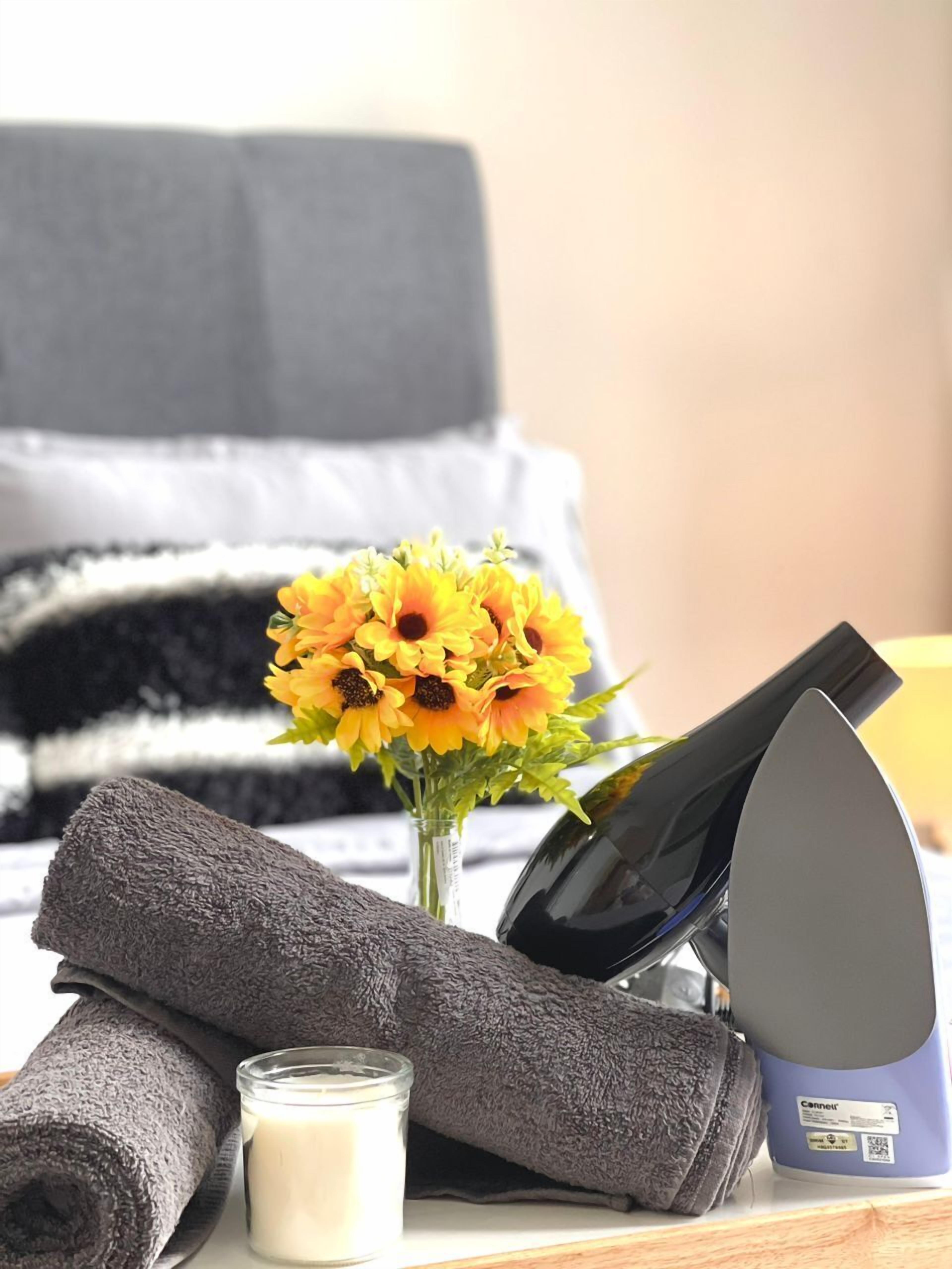 Una habitación ordenada con una cama, un secador de pelo, una vela y un florero con girasoles.